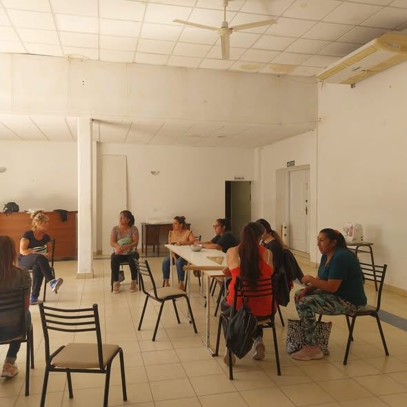 Grupo de personas sentadas alrededor de una mesa en el salón del Club de Leones durante una clase de costura